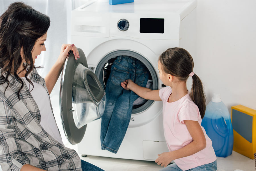 a mother and daughter put laundry into a gas-powered clothes dryer.